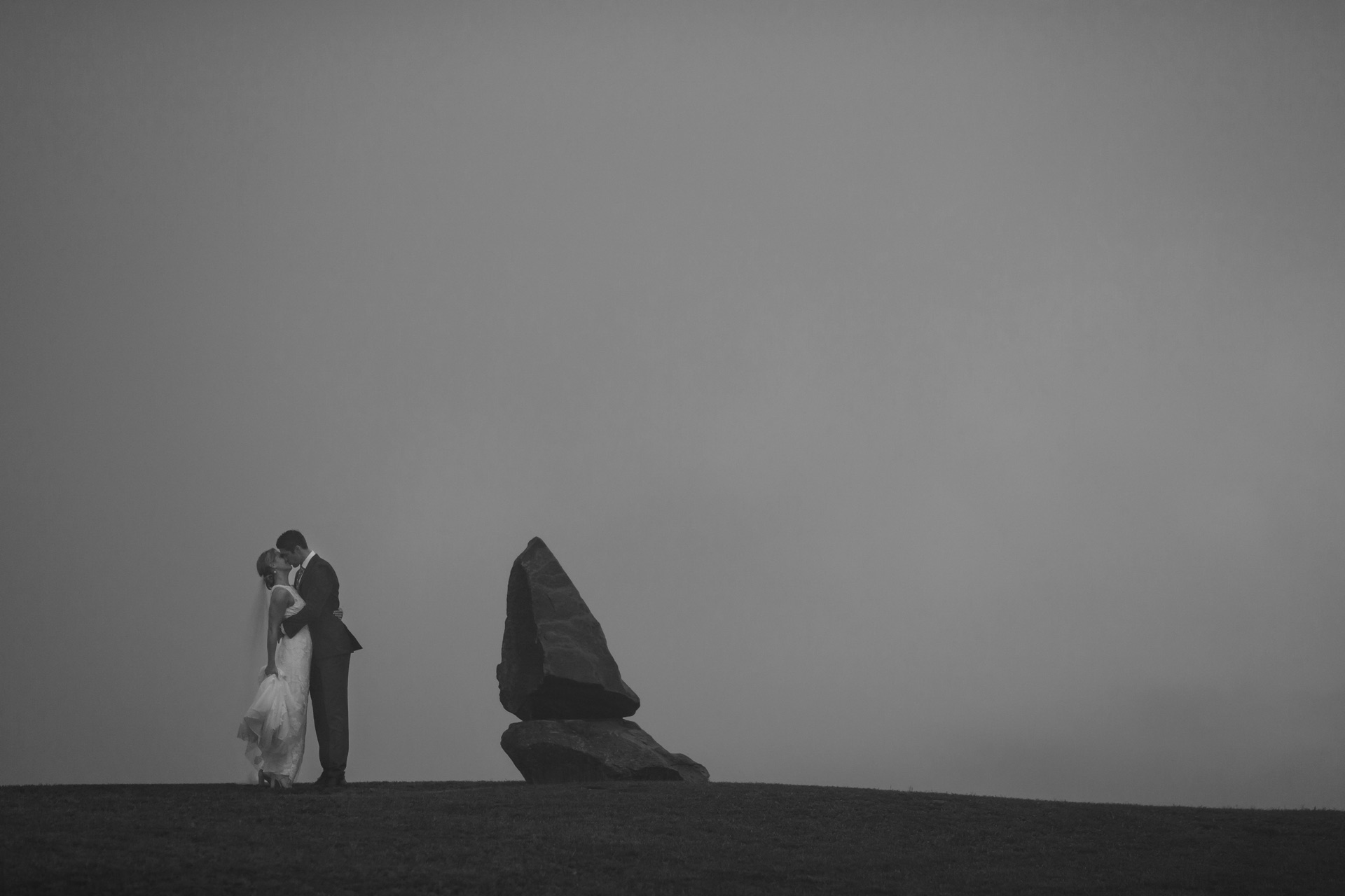 A couple dancing beside a sandstone sculpture in morning mist at Two Rivers